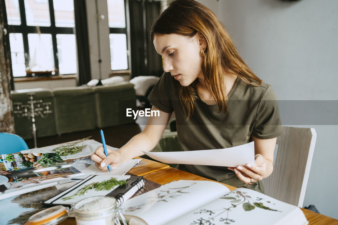 Female food stylist writing on paper while holding photograph in studio