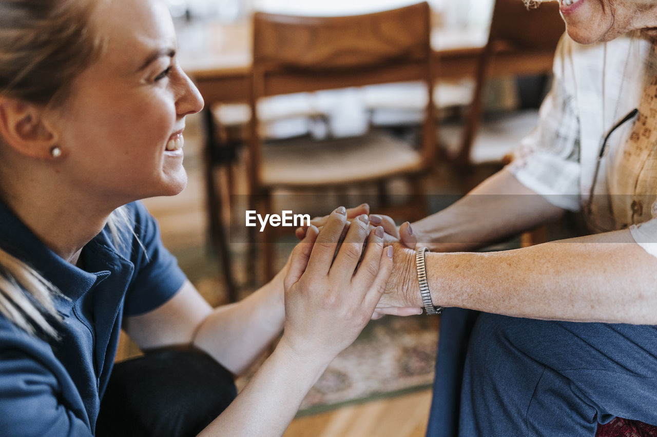 Smiling female healthcare worker holding hands of senior woman at home