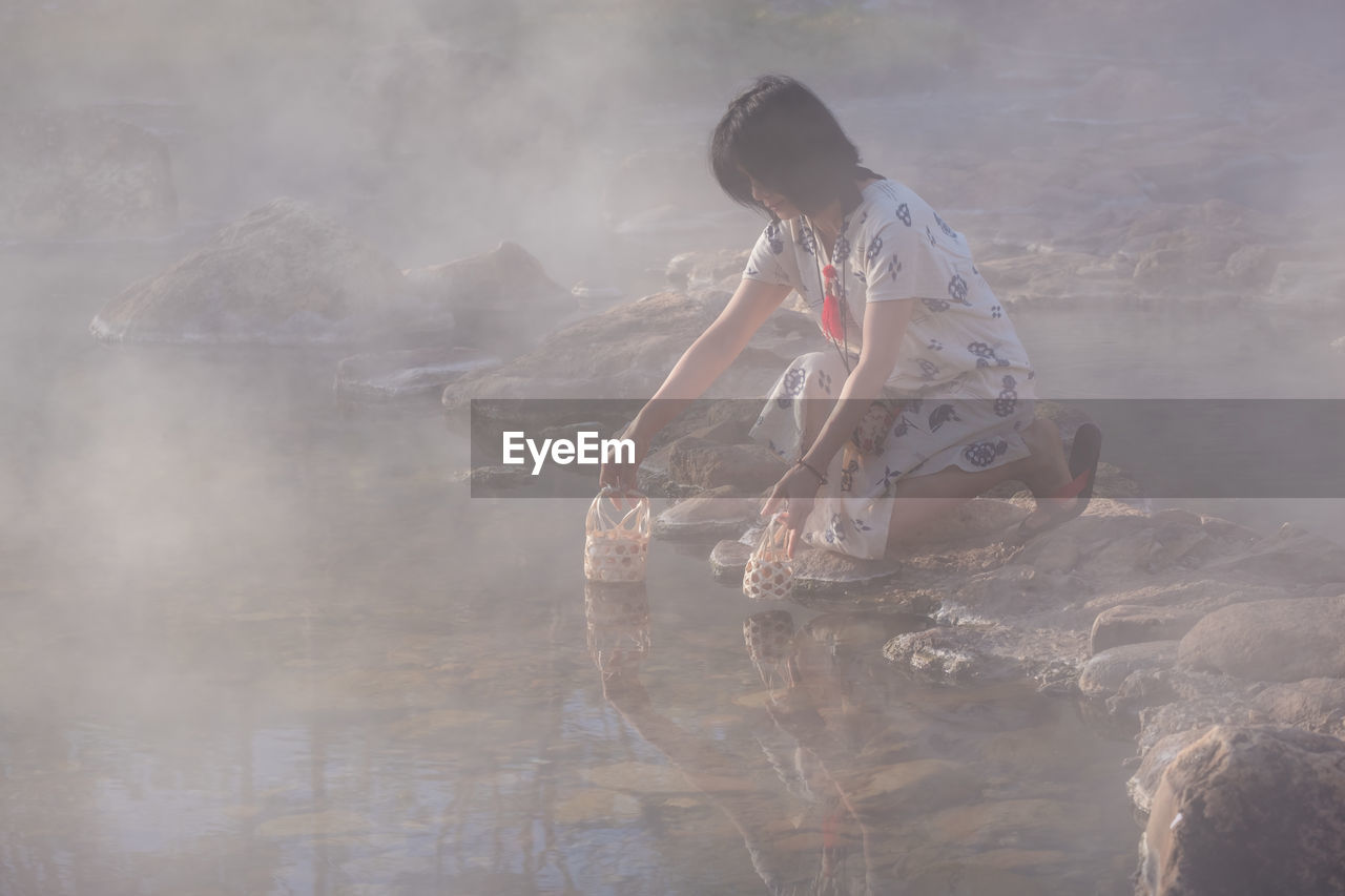 Side view of woman kneeling by hot spring