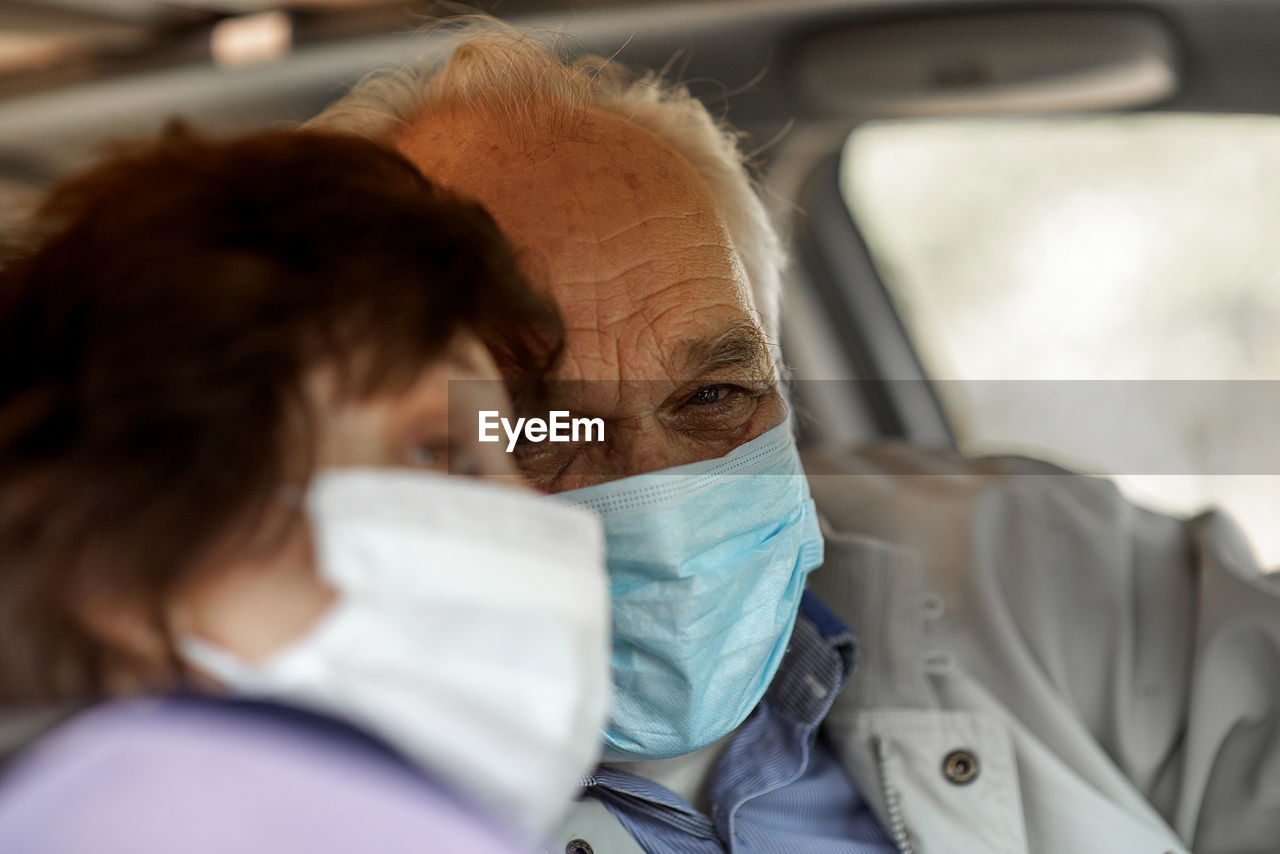 An elderly senior couple in medical face mask driving a car.  travel and old people concept