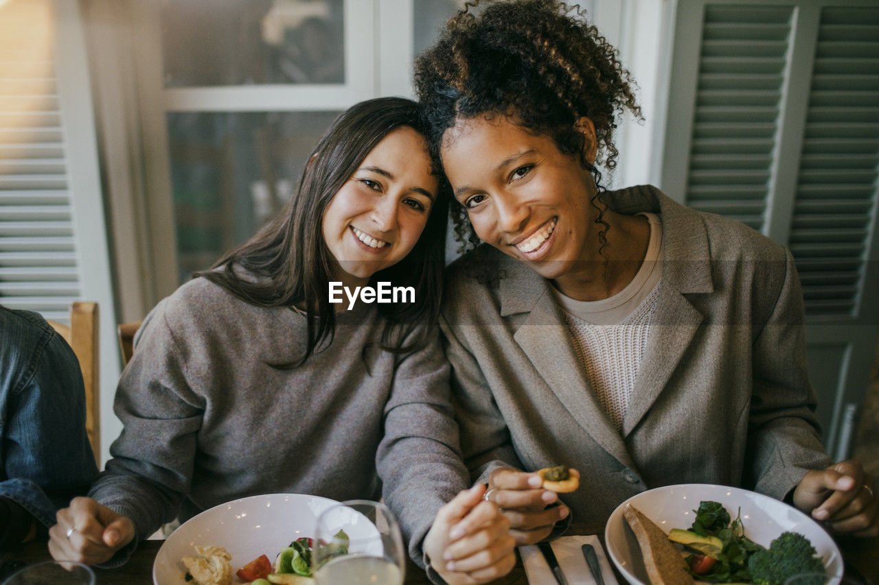 Portrait of smiling young female friends sitting at dining table in patio for dinner party