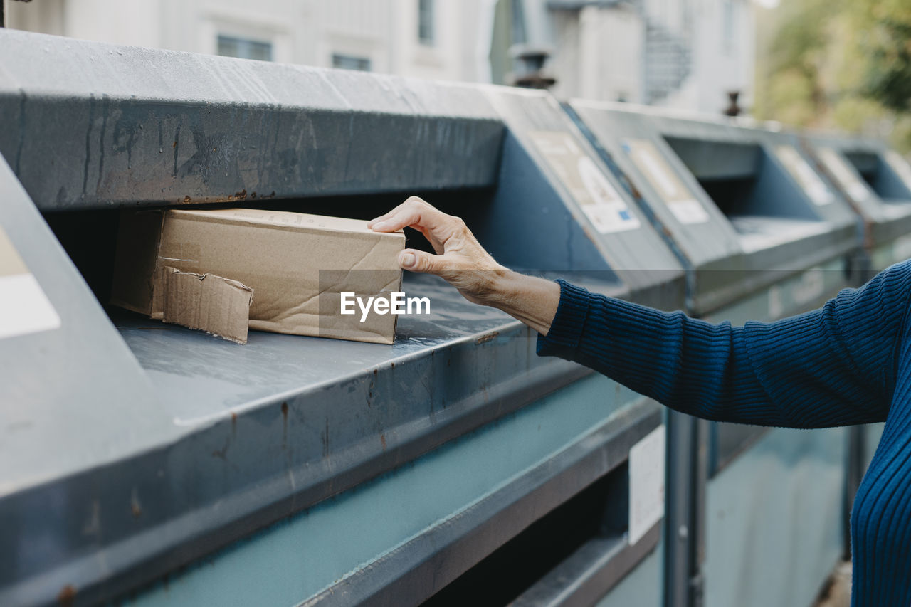 Woman's hand putting cardboard box into recycling bin