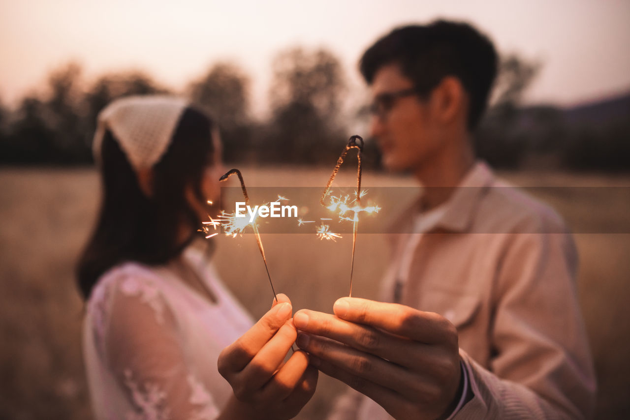 Couple holding sparkler while standing on field