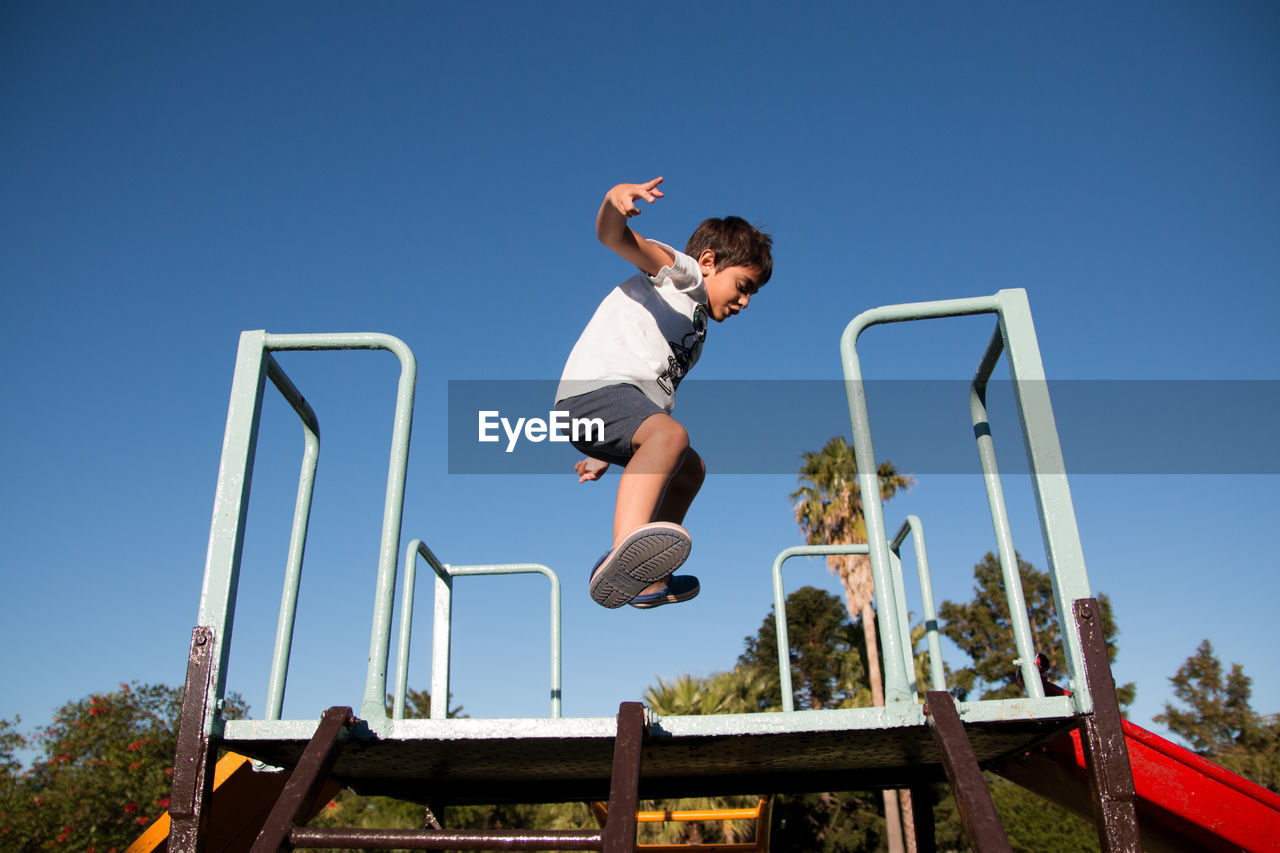 Low angle view of boy jumping on slide against clear sky