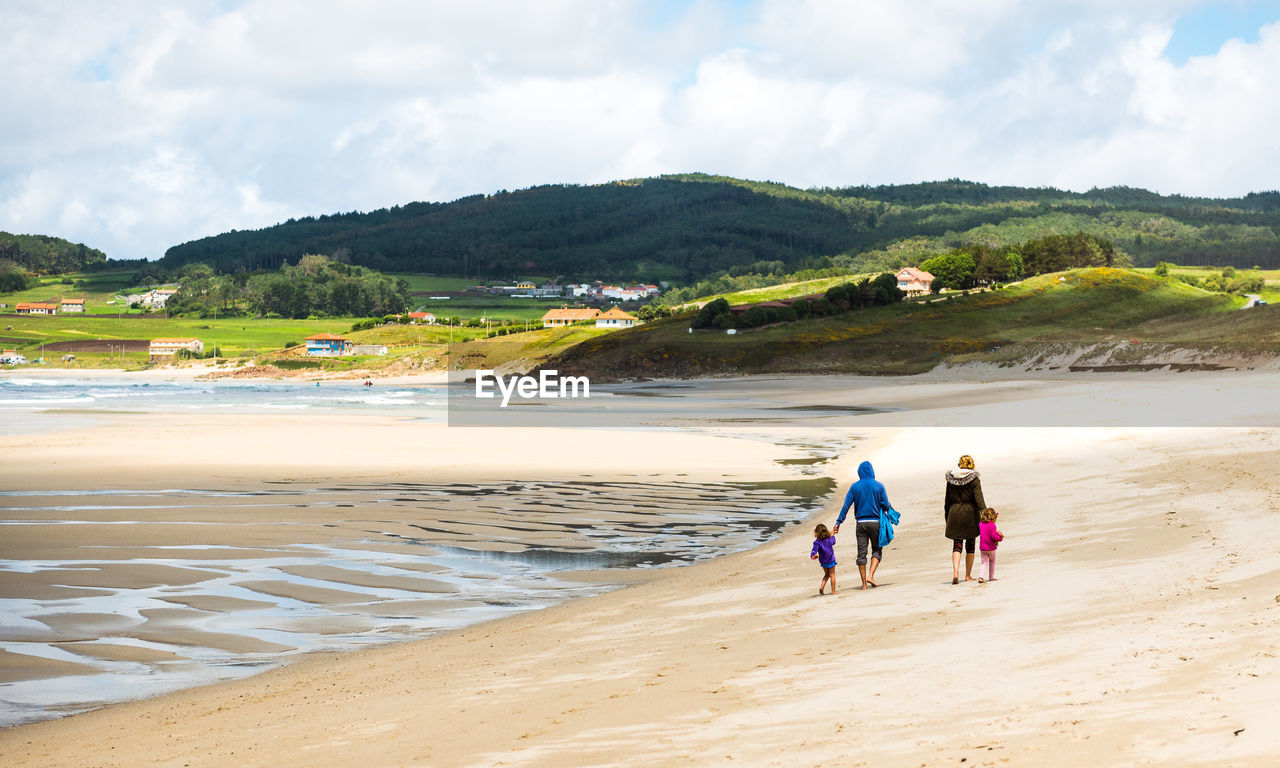 Rear view of people walking at beach against sky