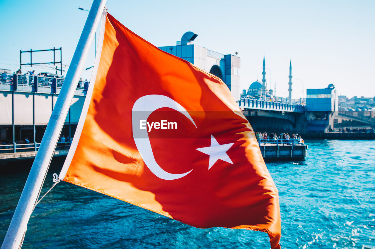 Red turkey flag with star and moon on boat against sky