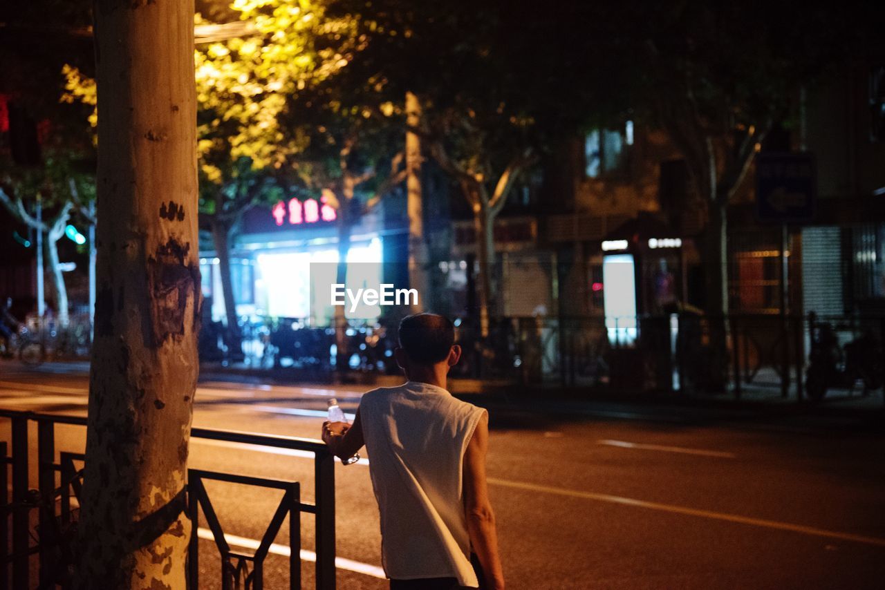 Rear view of man standing on footpath at night