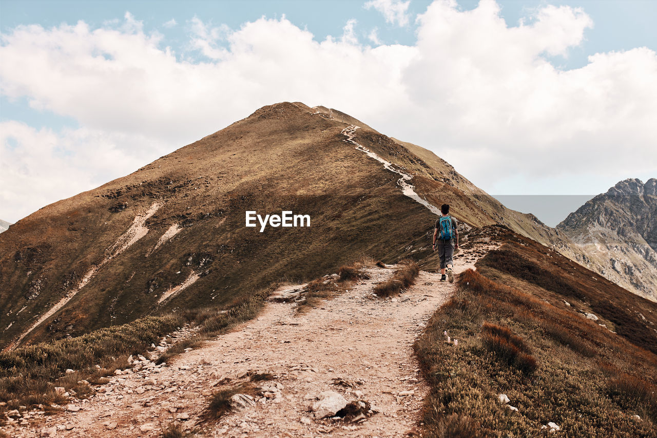 Young man with backpack hiking in a mountains, actively spending summer vacation