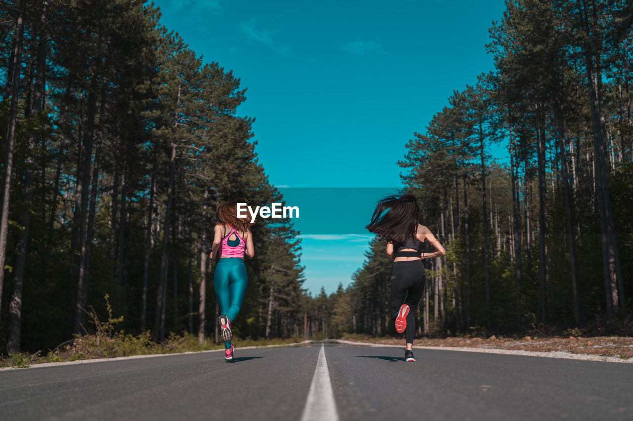 Rear view of woman running on road against trees