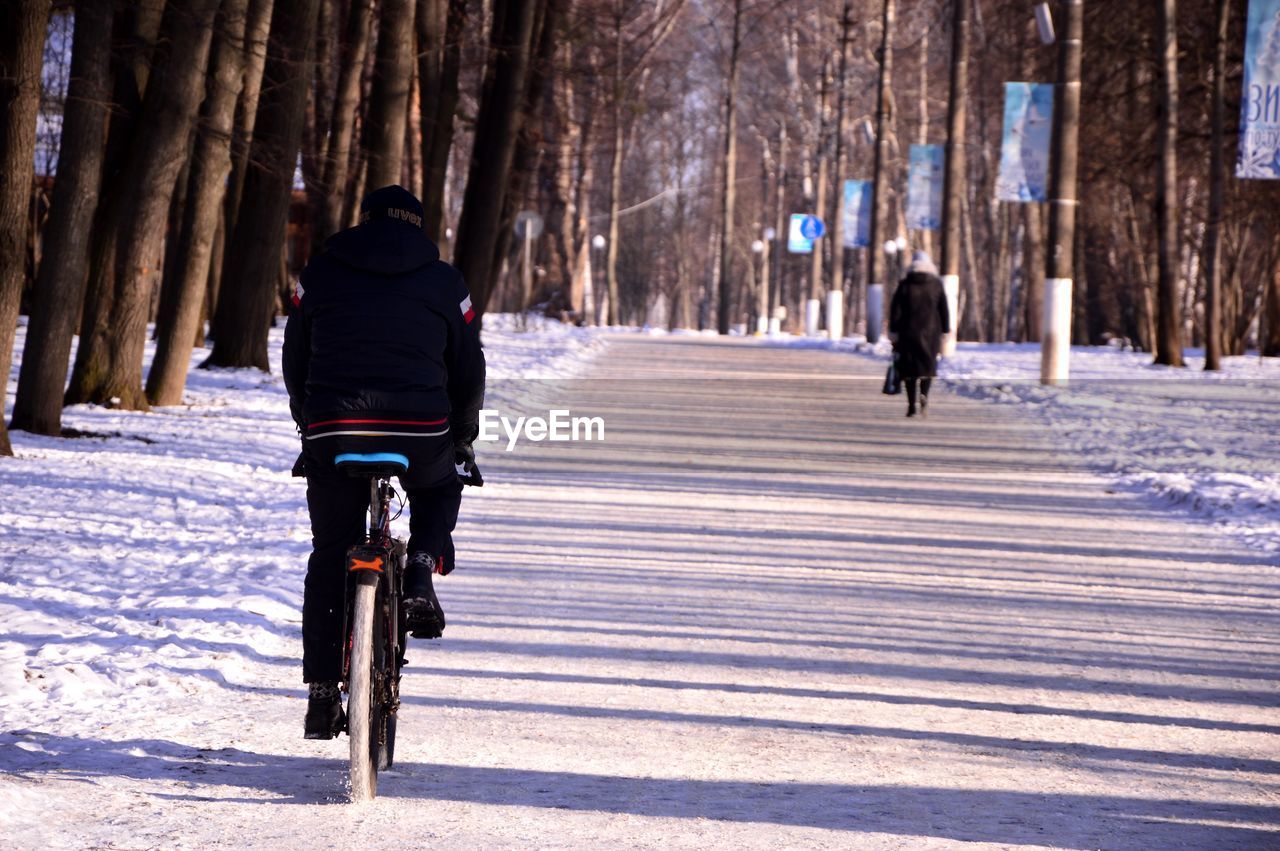 REAR VIEW OF WOMAN RIDING BICYCLE ON SNOW COVERED