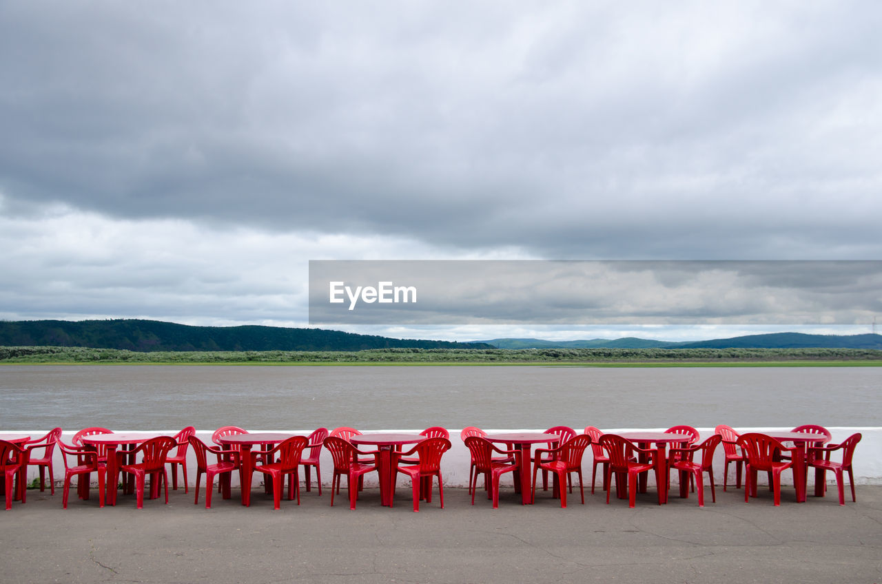 Cafe outdoors. red plastic tables and chairs by the river on a background of hills.