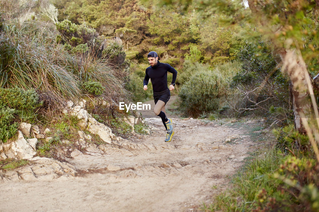 Active man running on dirt road in forest at morning