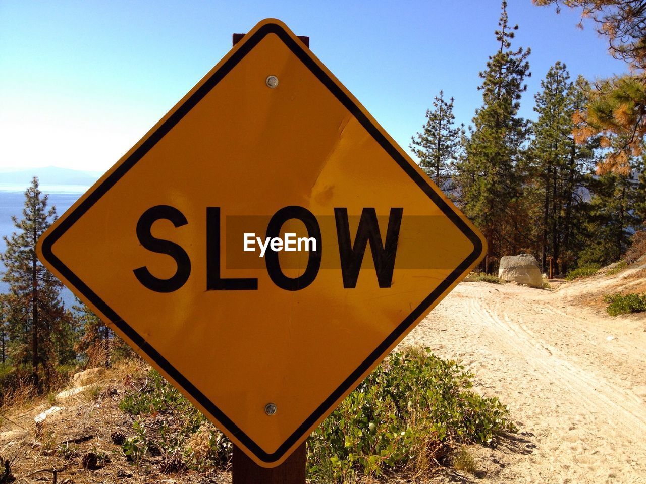 Close-up of slow sign by dirt road against blue sky