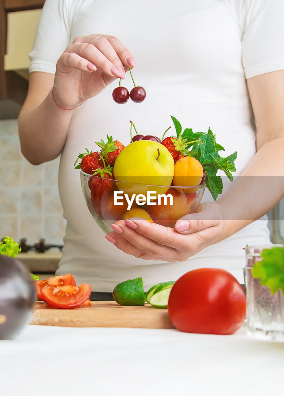 Midsection of pregnant woman with bowl of fruits