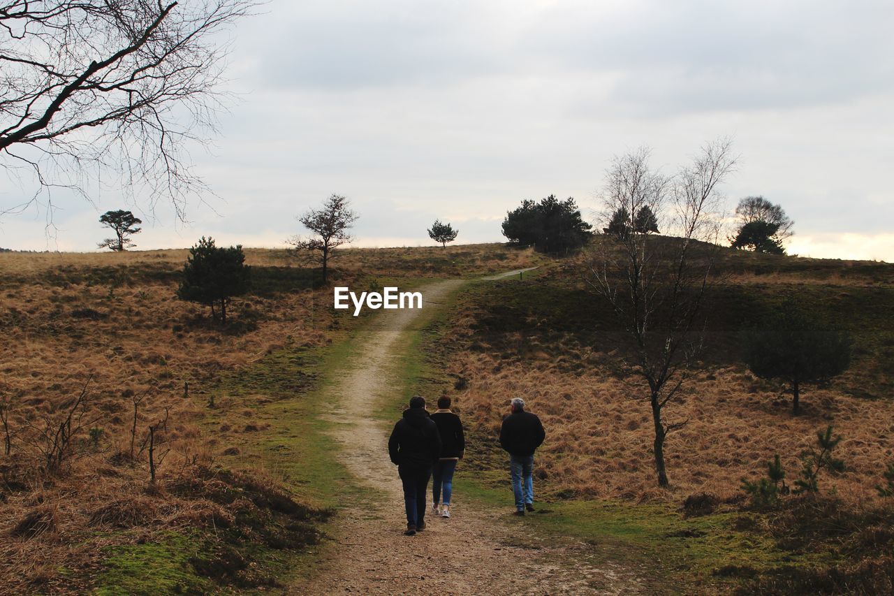 Rear view of men walking on dirt road against sky