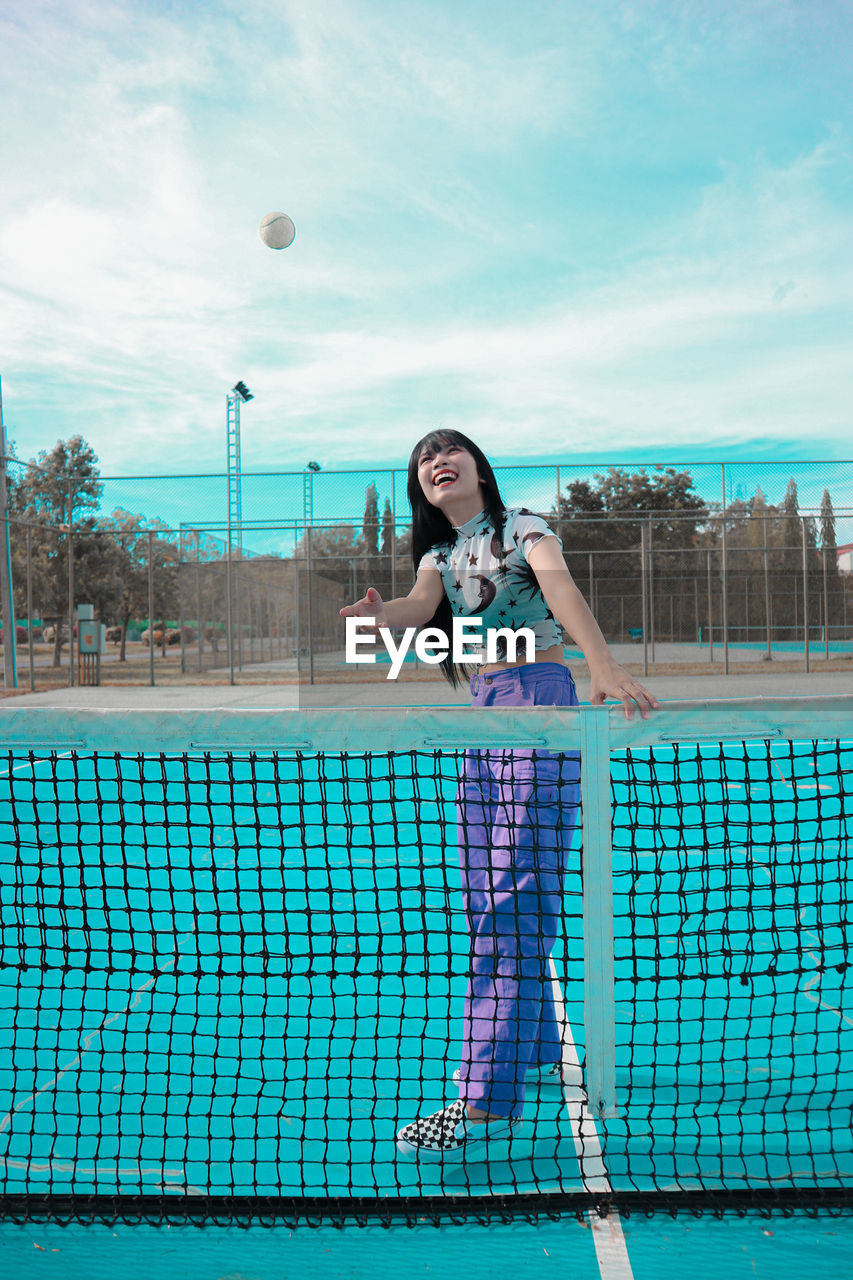 Full length portrait of woman standing in tennis courts