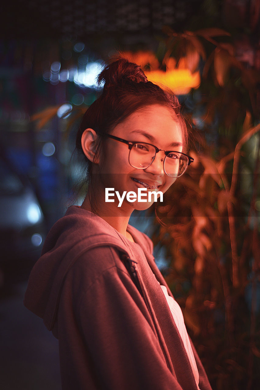 Portrait of smiling young woman wearing eyeglasses at night