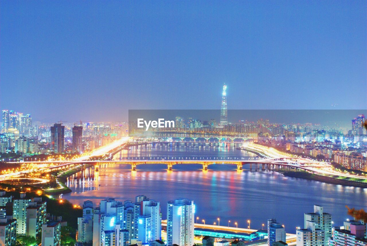 Bridge over river against sky in illuminated city at night