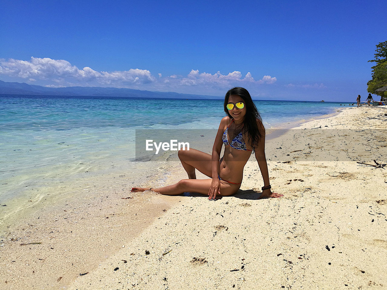 Portrait of woman wearing bikini sitting at beach against sky