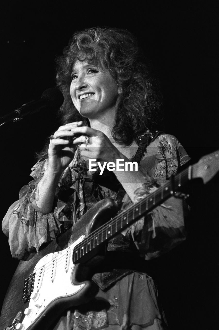 PORTRAIT OF A SMILING WOMAN PLAYING GUITAR