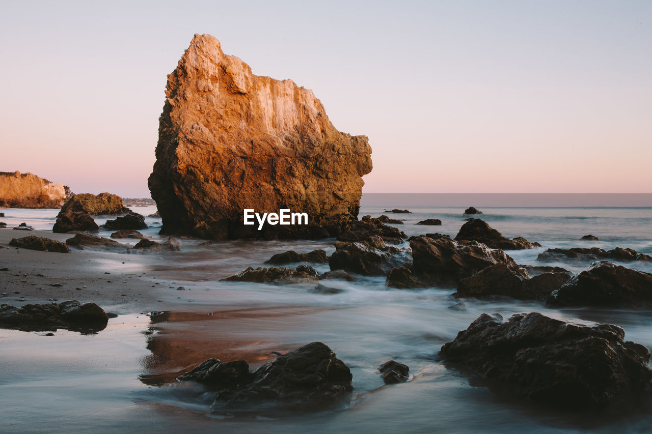 View of rocks at calm sea against clear sky