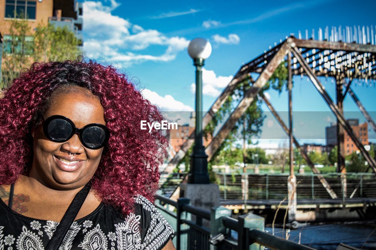 Portrait of woman with curly maroon hair while wearing sunglasses in city