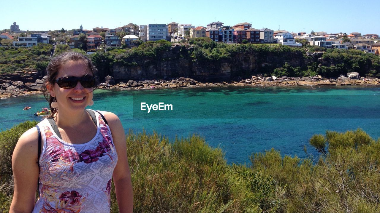 PORTRAIT OF SMILING MID ADULT MAN WEARING SUNGLASSES AT WATER