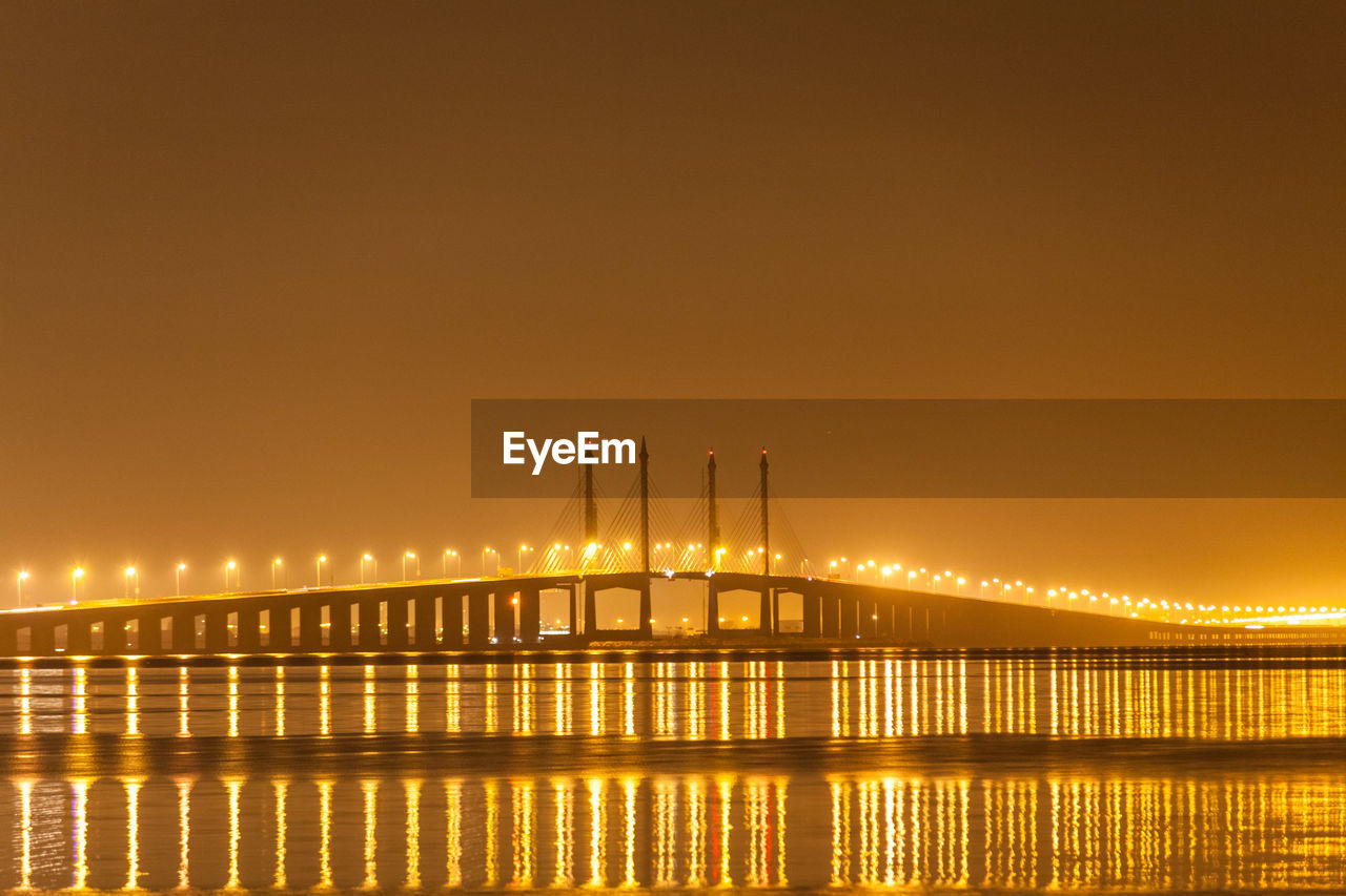 Illuminated bridge over sea against sky at night