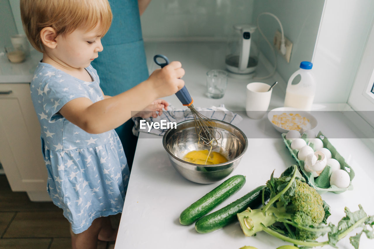 Toddler little daughter helps mom cook dinner.