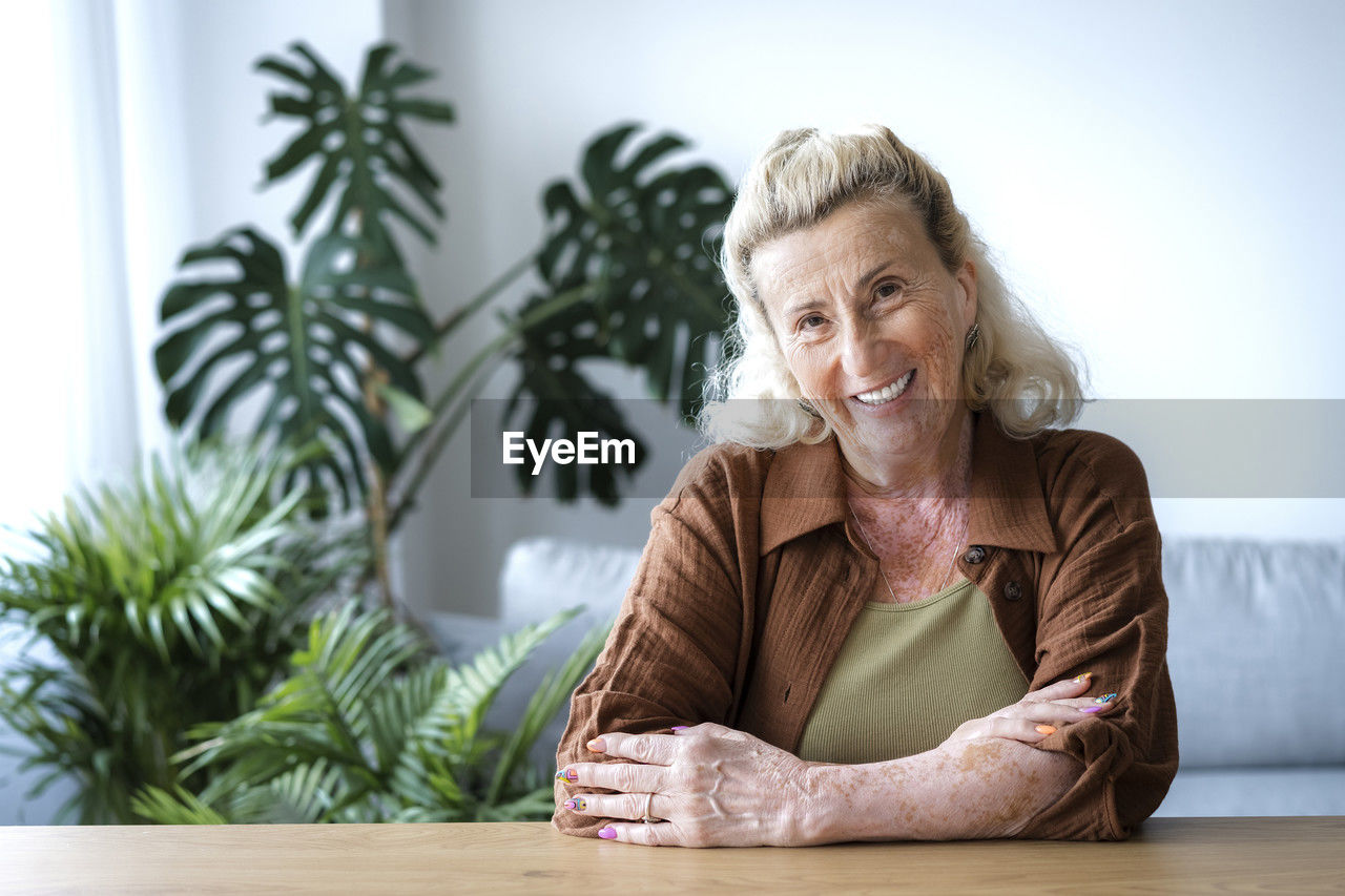 Happy elderly woman with arms crossed at home