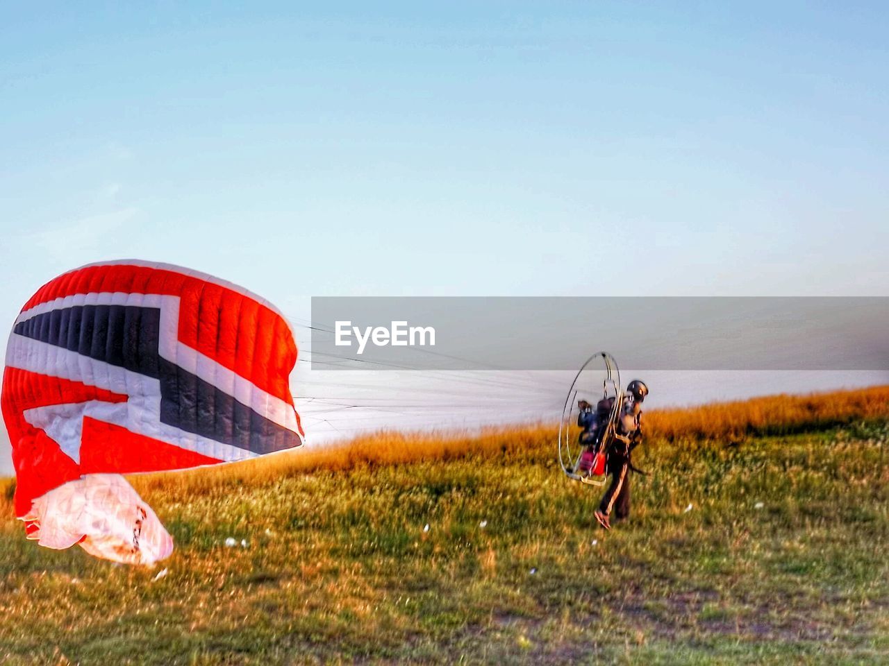 Man with powered parachute on grassy field against clear sky during sunset