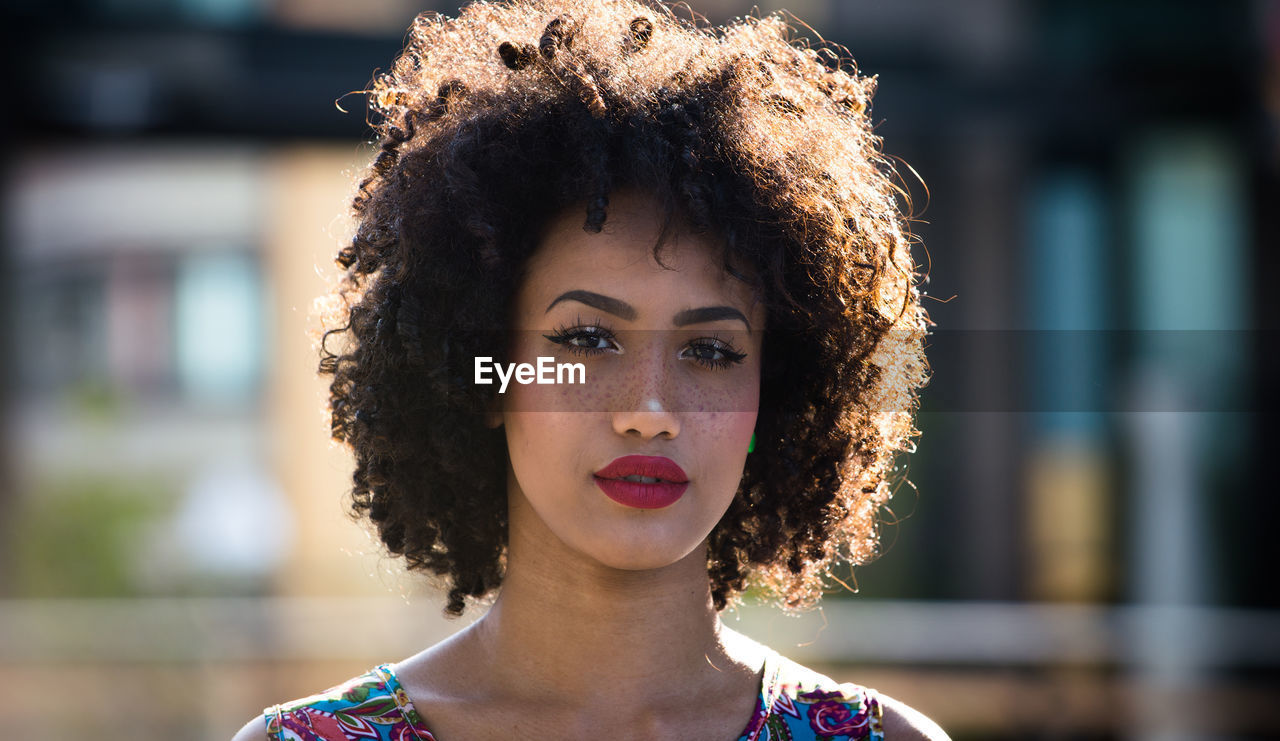 Portrait of fashionable young woman with curly hair in city