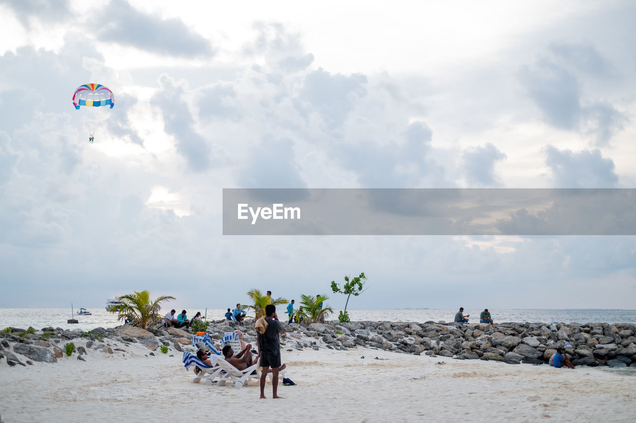 PEOPLE ENJOYING ON BEACH AGAINST SKY