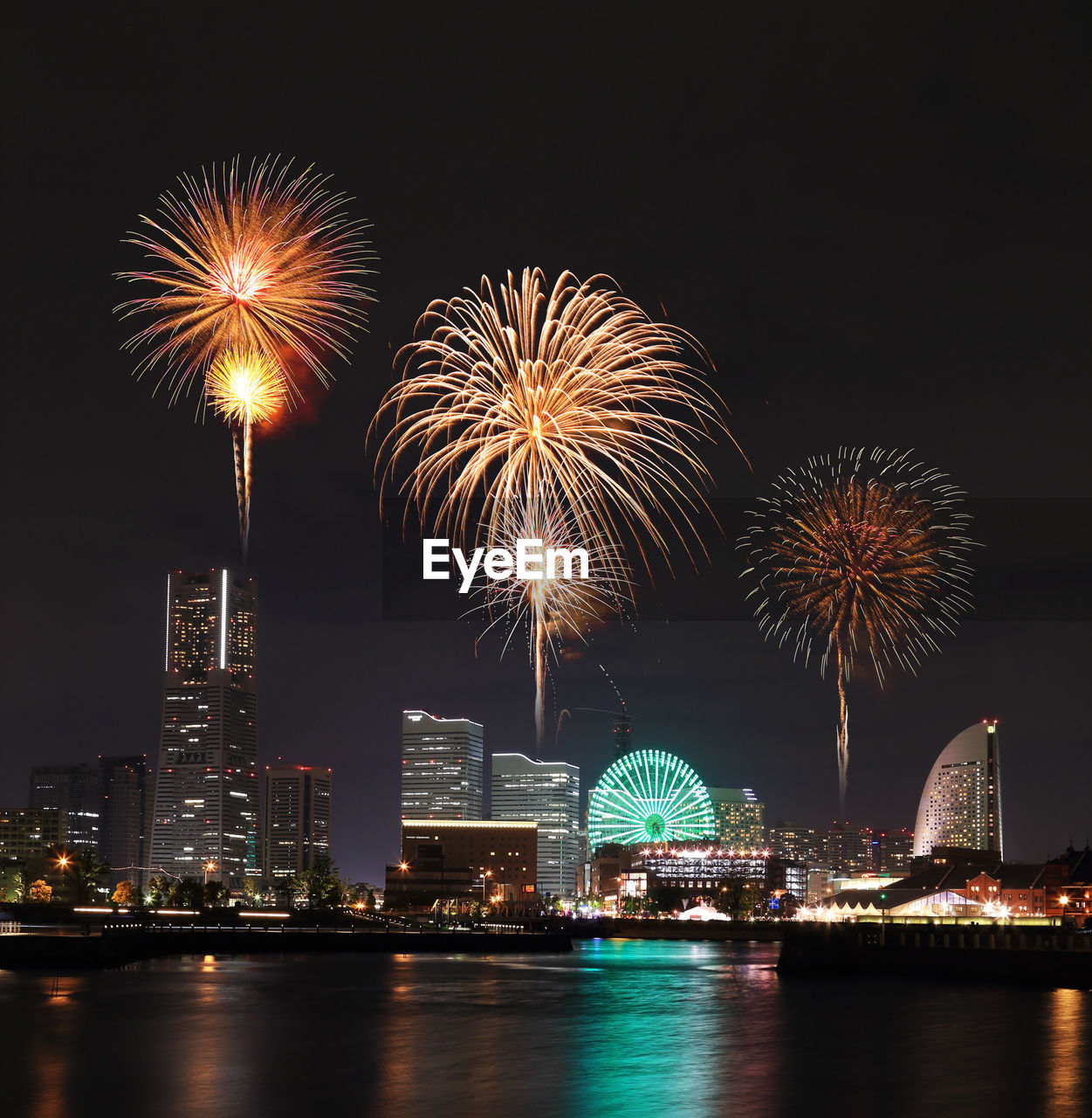Firework display over river and illuminated cityscape at night