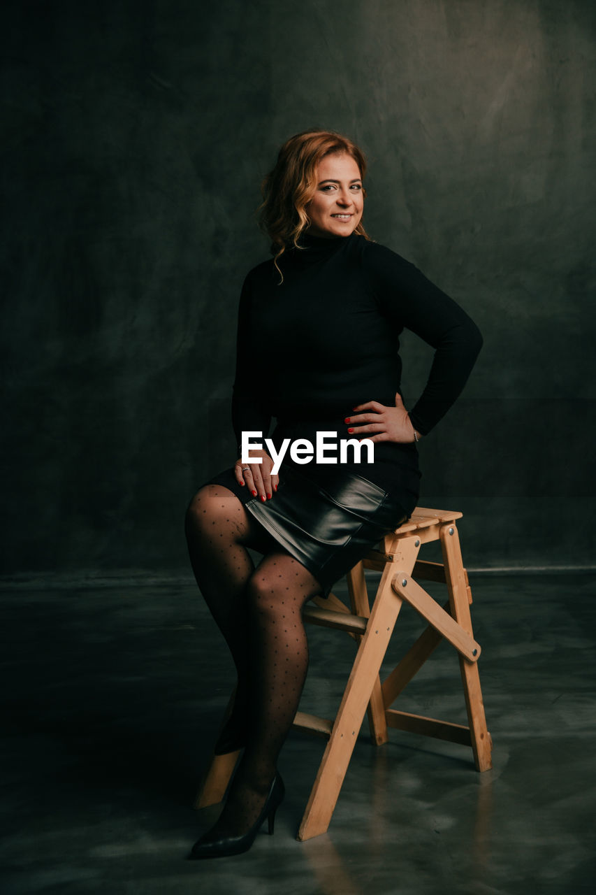 Portrait of woman sitting on chair against wall