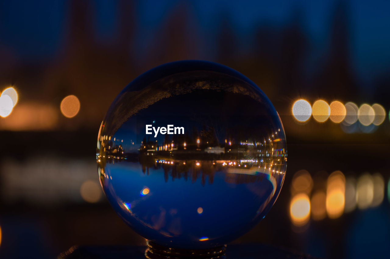 Illuminated buildings and river seen through crystal ball at dusk