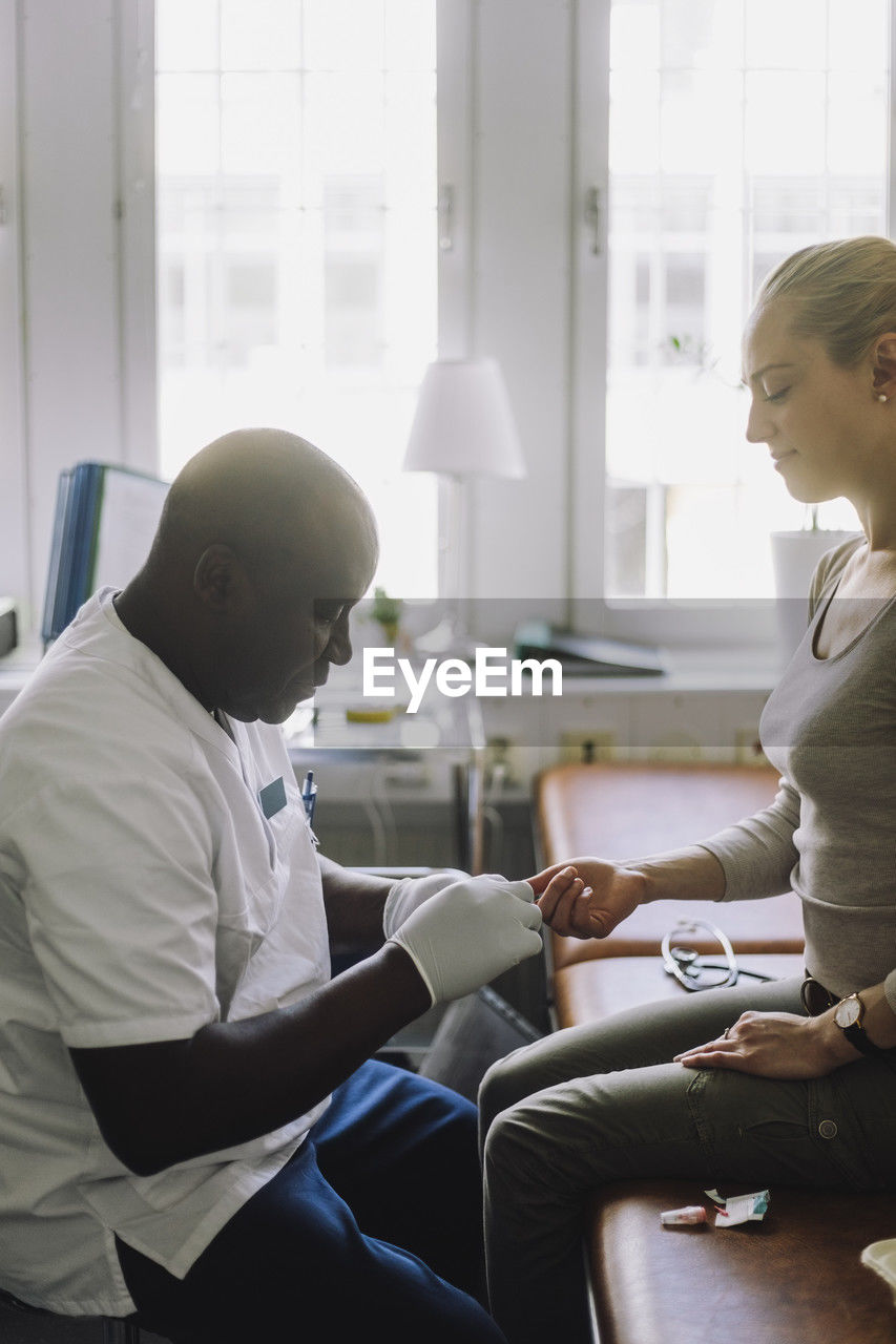 Side view of male doctor checking blood sugar level of patient sitting in clinic