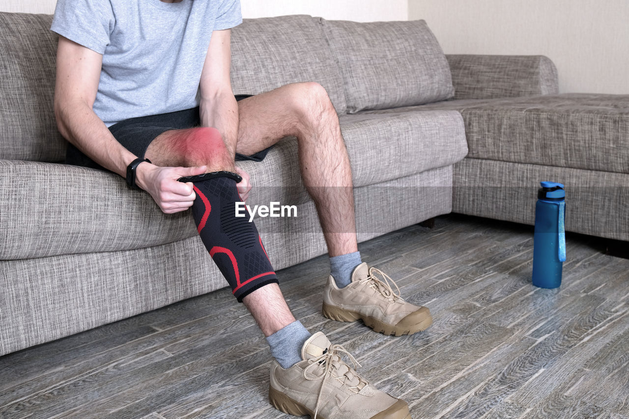 low section of man tying shoelace while sitting on hardwood floor