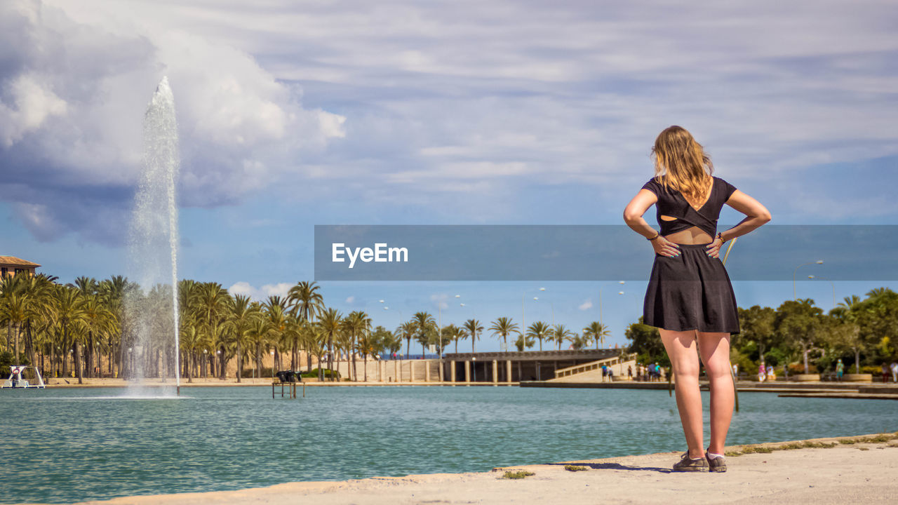 Rear view of woman looking at fountain against sky