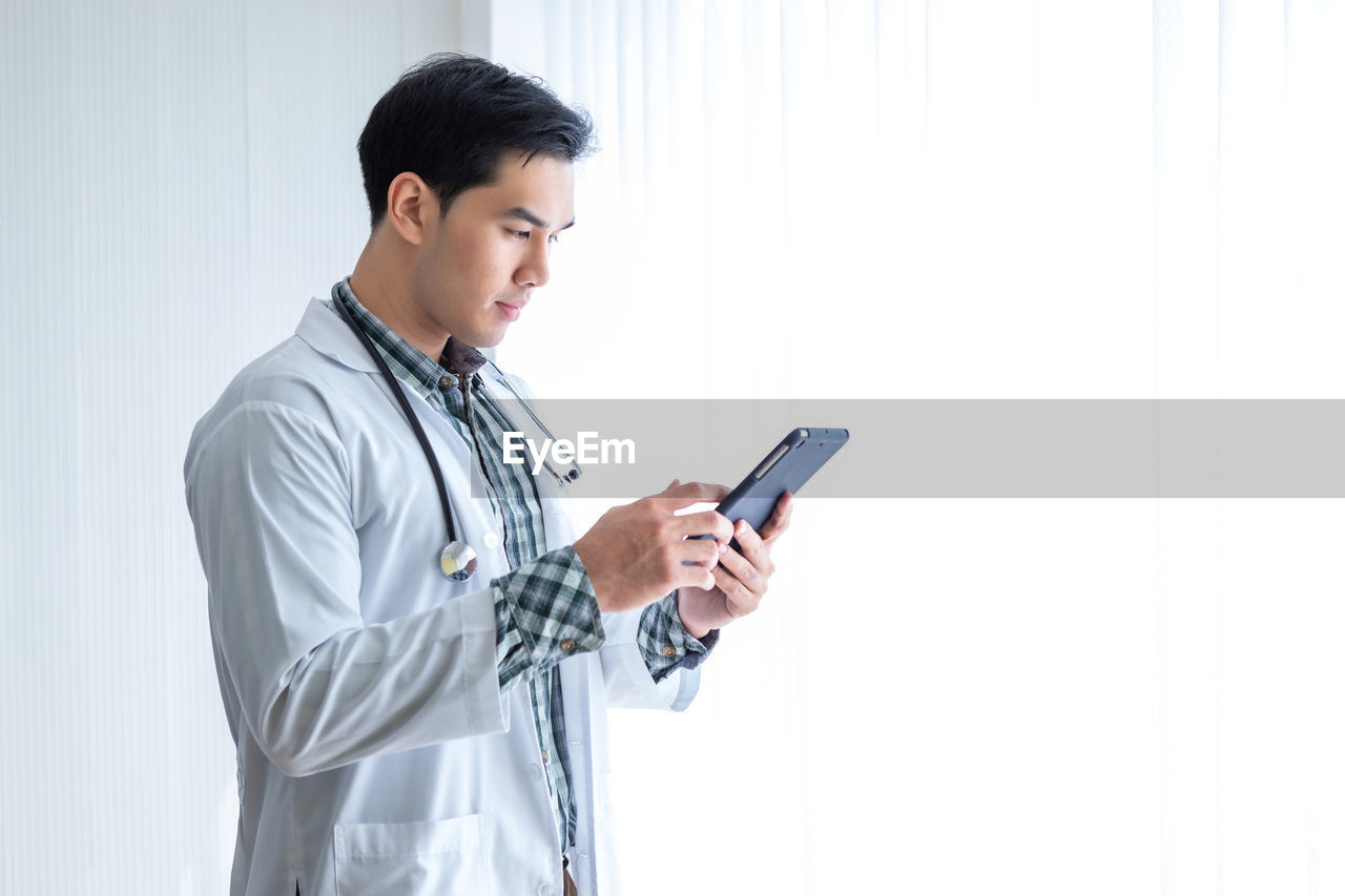 SIDE VIEW OF YOUNG MAN USING MOBILE PHONE IN LAPTOP