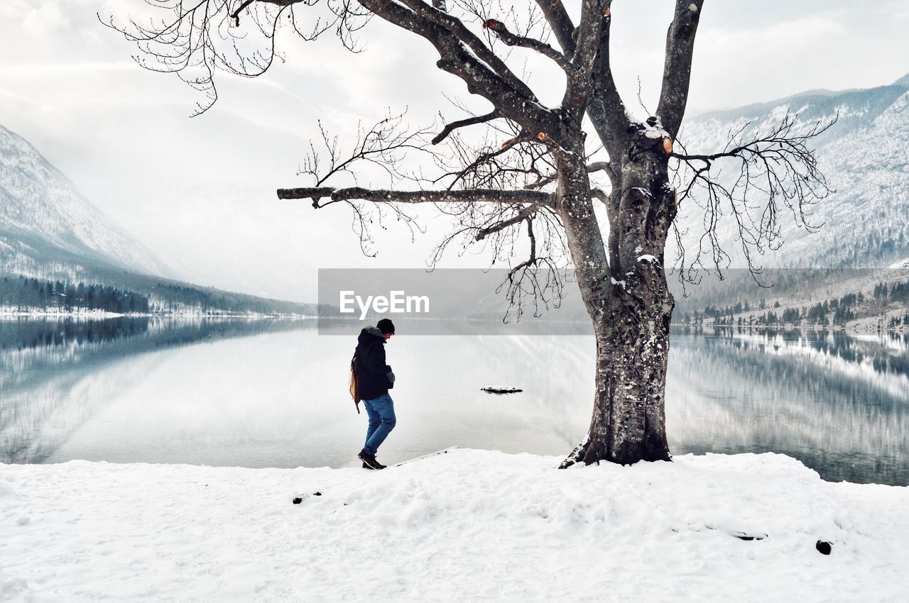 Full length of man walking on snow covered land by lake