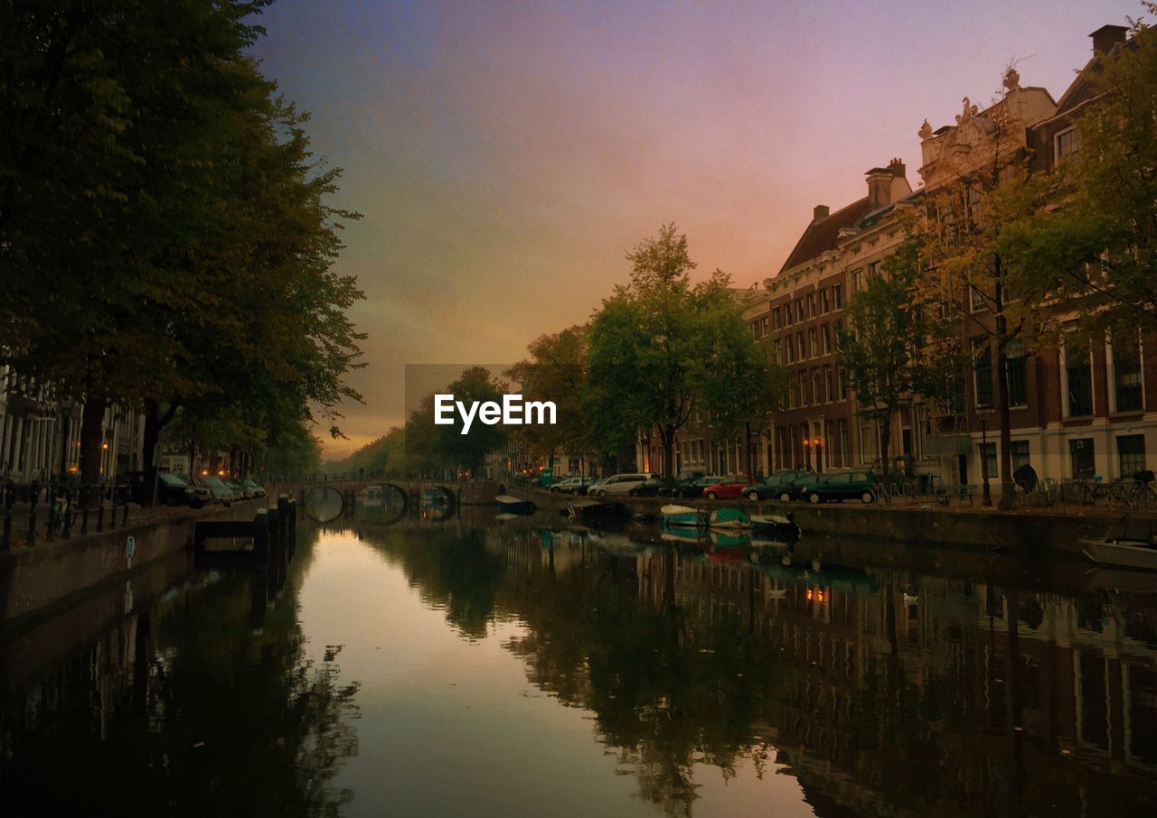 Canal by buildings against sky during sunset