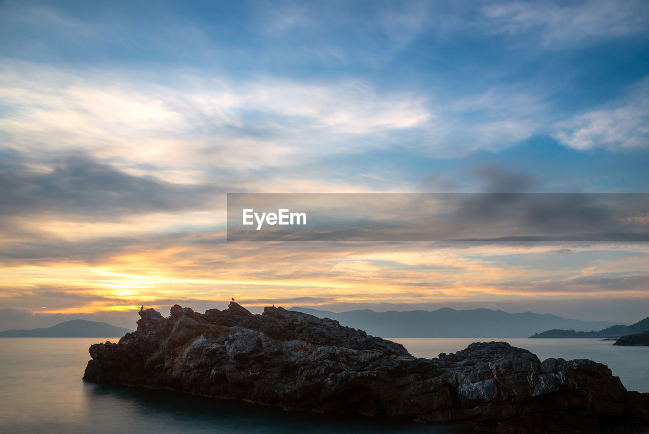 Rock formations by sea against sky during sunset