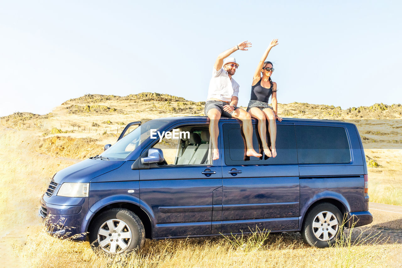 A couple waving to their friends on top of a van