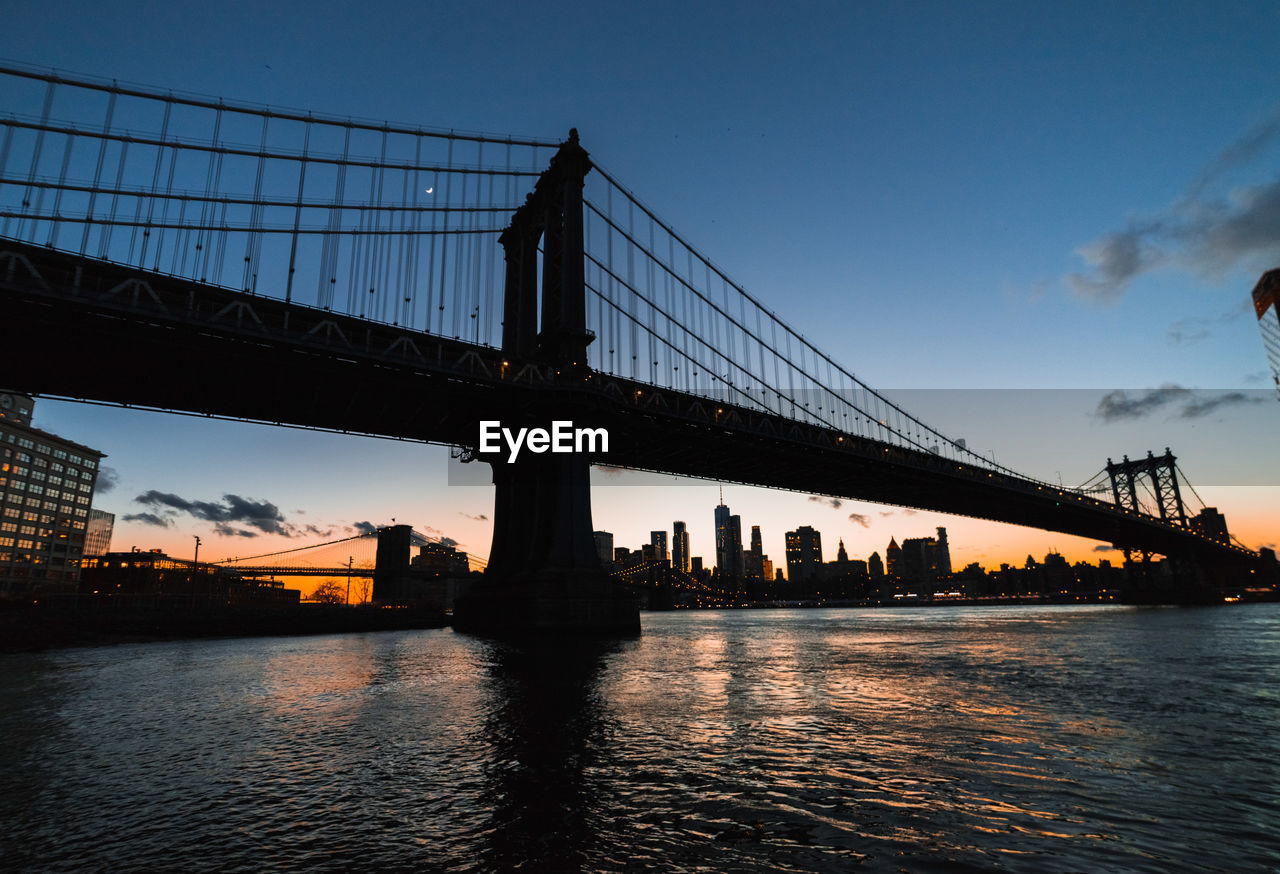 Silhouette of suspension bridge over river during sunset