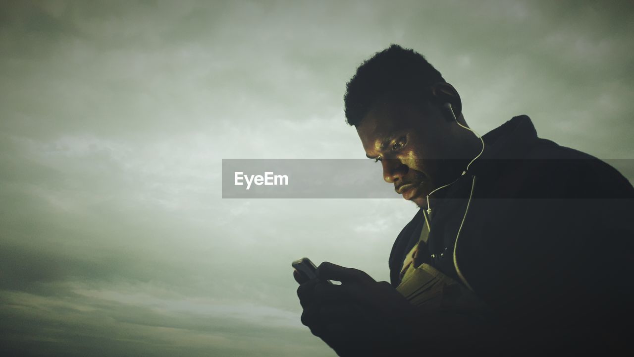 LOW ANGLE VIEW OF PERSON USING MOBILE PHONE AGAINST SKY