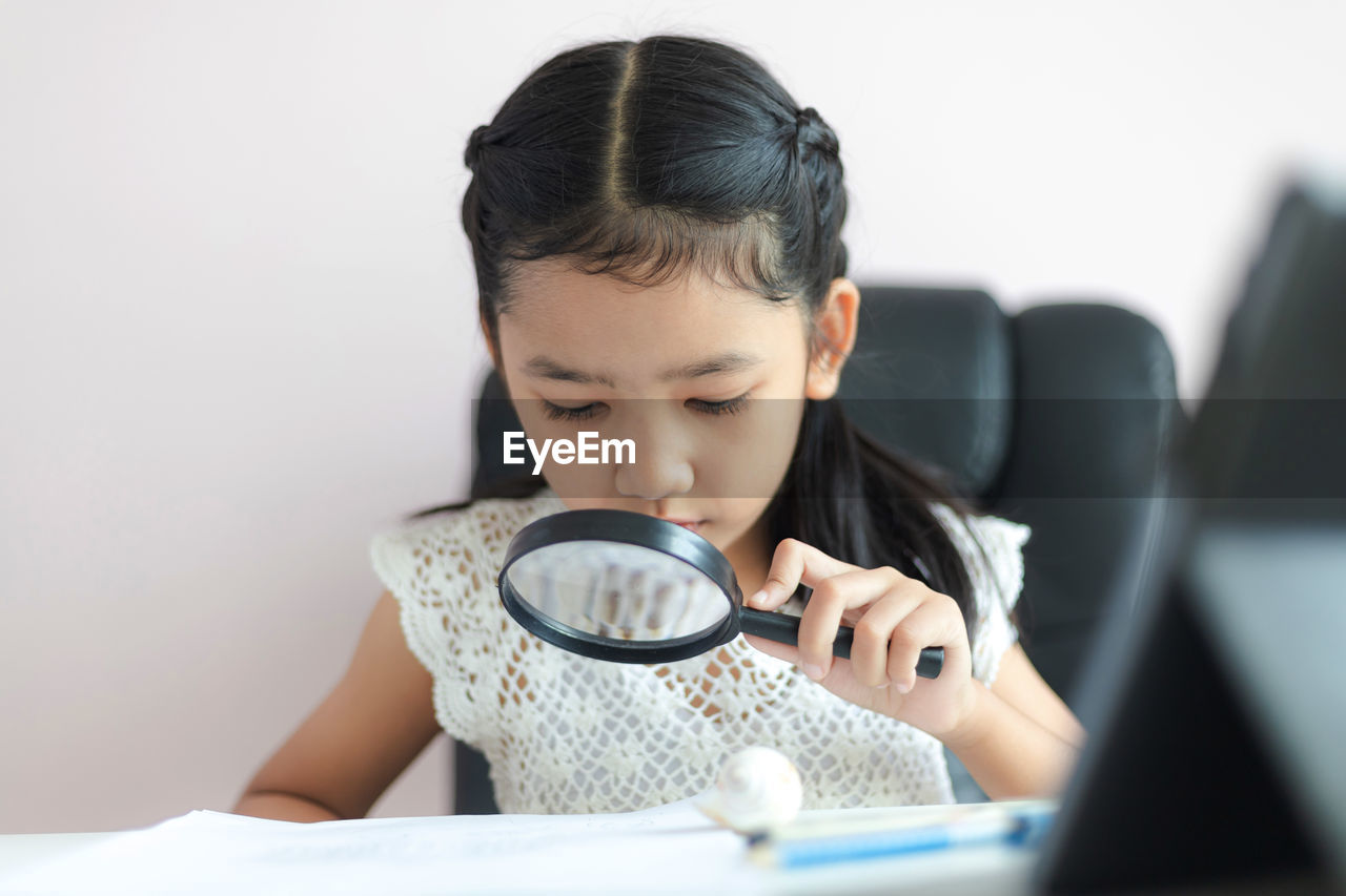 Girl holding magnifying glass on table