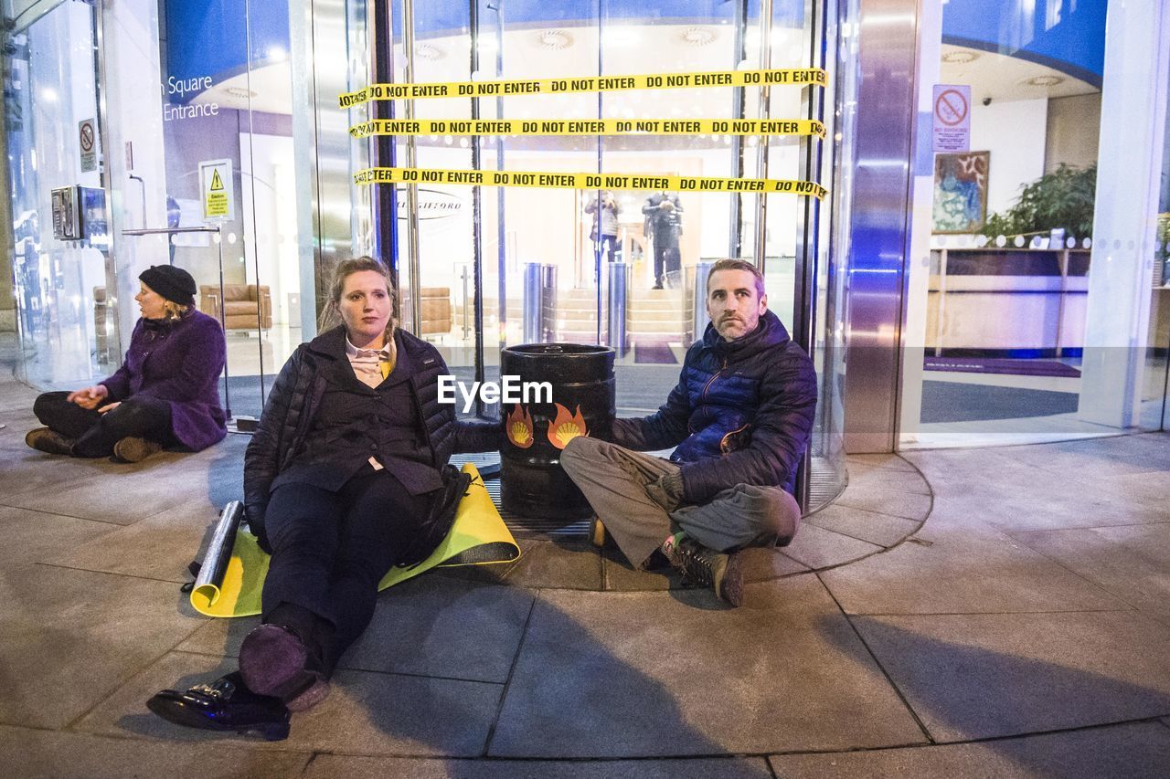 GROUP OF PEOPLE SITTING ON FLOOR IN CORRIDOR