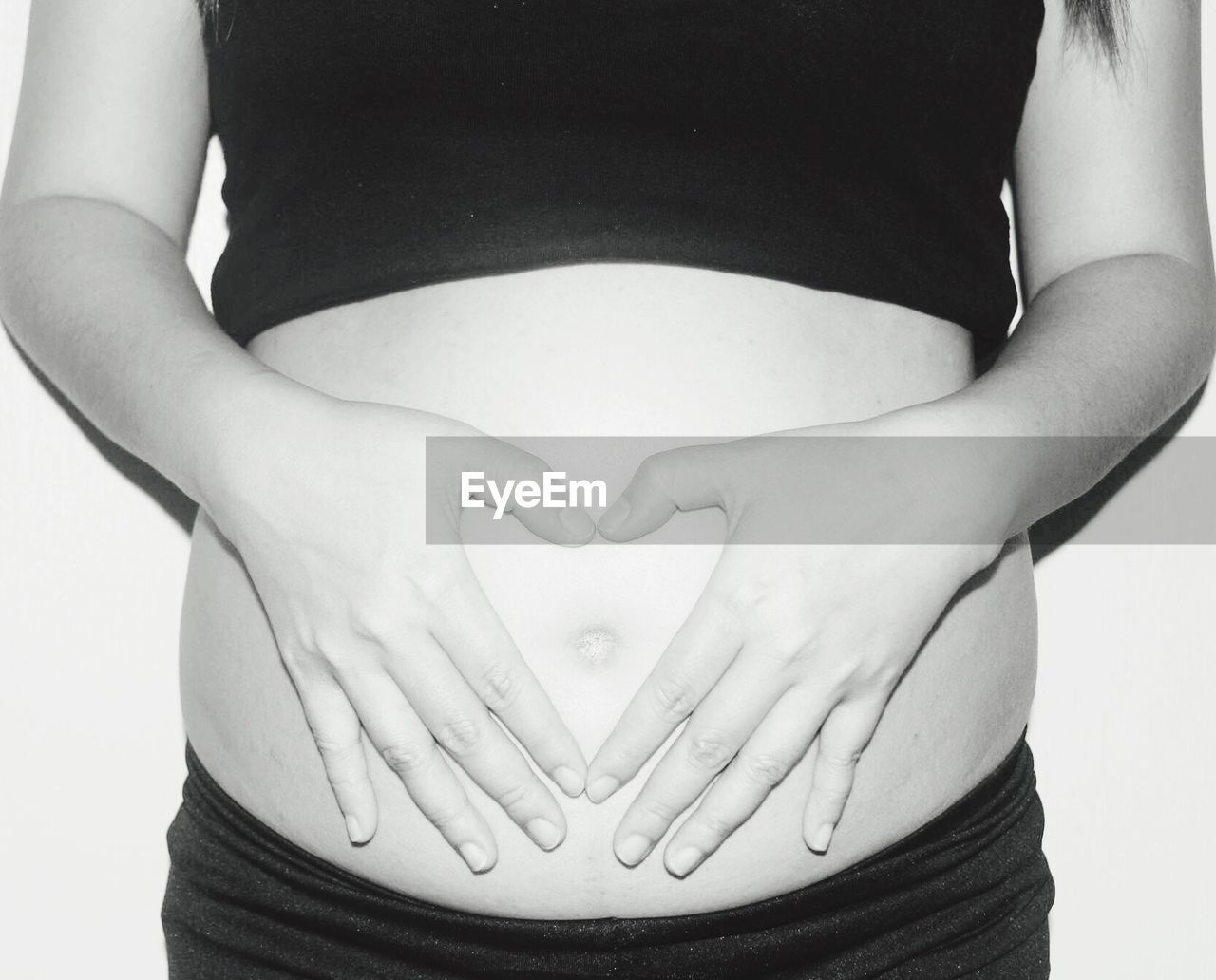 Midsection of pregnant woman forming heart shape with hands on belly