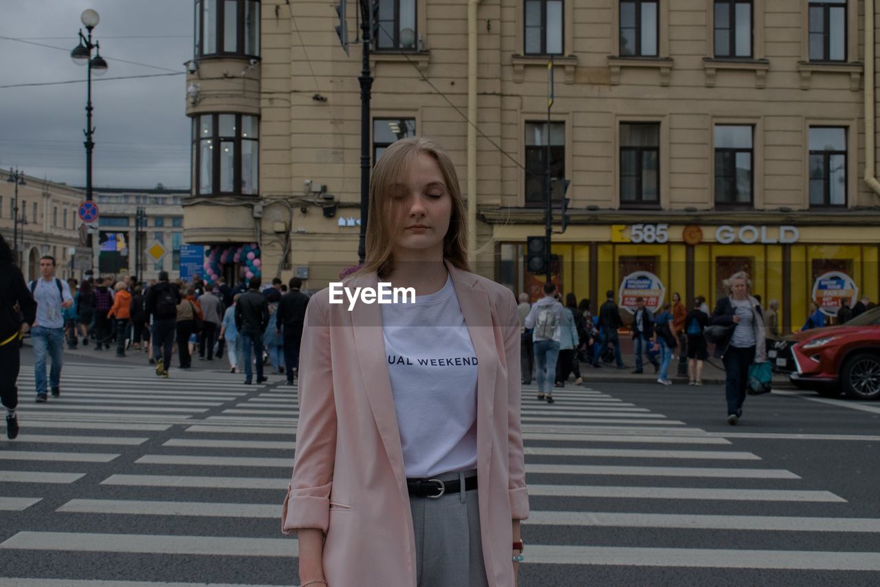 Young woman with eyes closed standing on zebra crossing in city